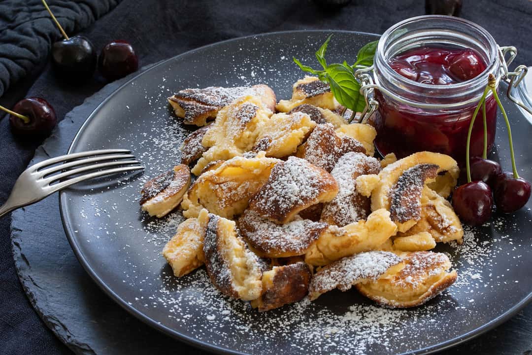 Scrambled pancakes (Kaiserschmarrn) with cherries on a plate and strawberry jam