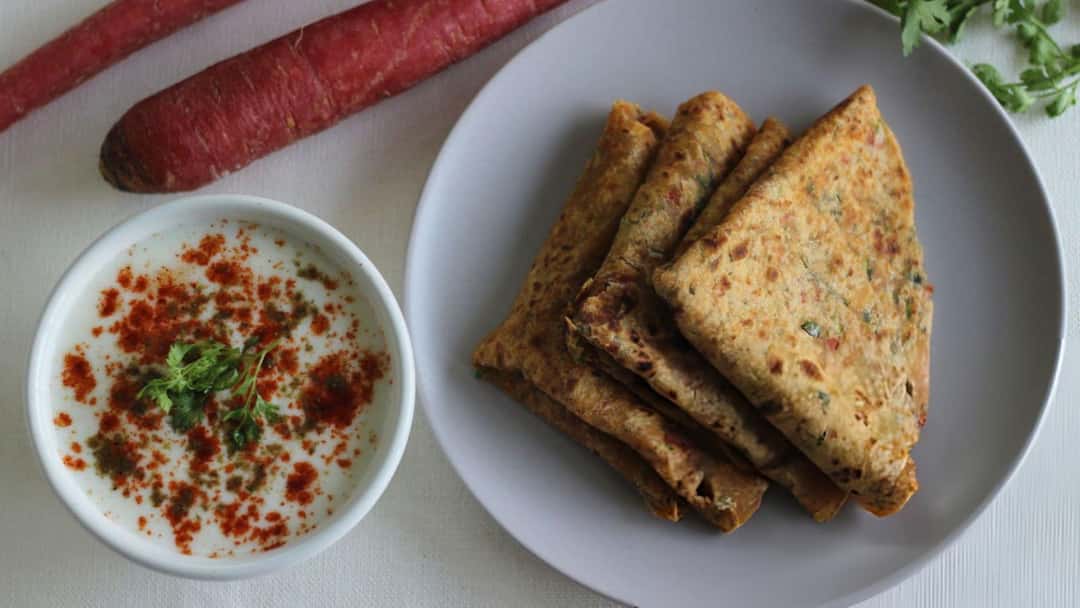 Golden and crispy carrot and garlic stuffed paratha on a plate with a side
