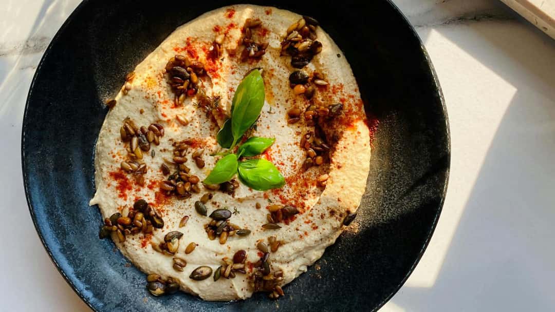 Top view of a person holding a dish of jackfruit seed hummus. (banner image)