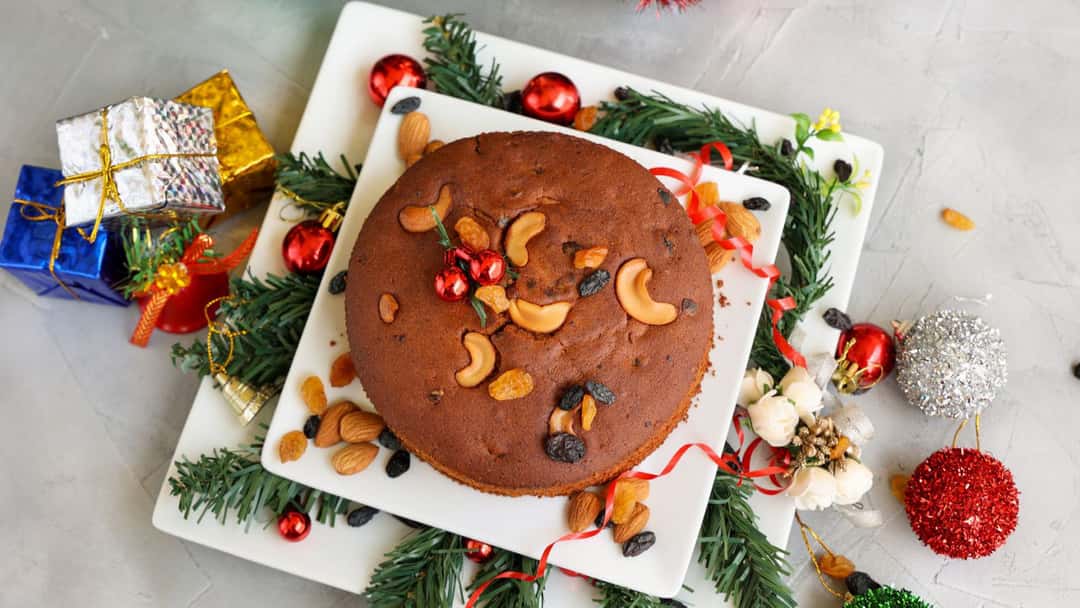 Kerala plum cake topped with cashews and dried fruits on a plate. (banner image)