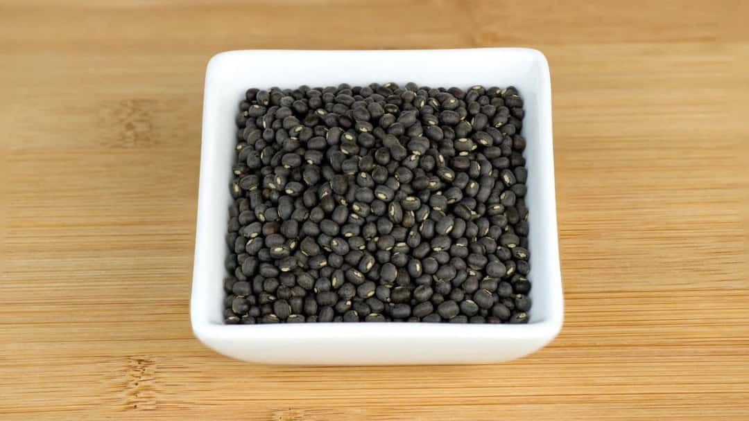 Close-up of raw black urad dal (whole black gram) with skin.