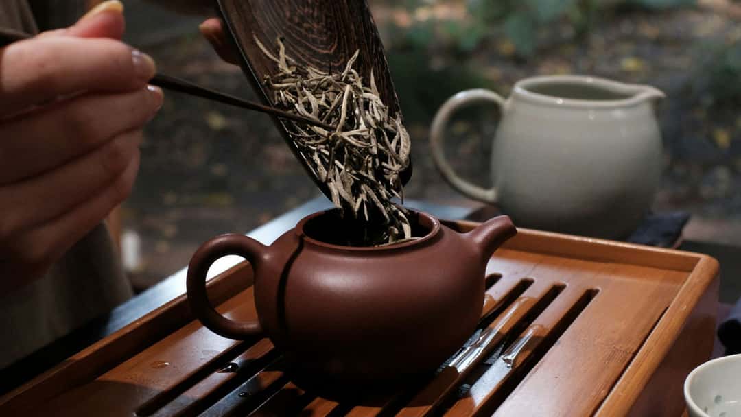Tea leaves being put inside a tea pot.