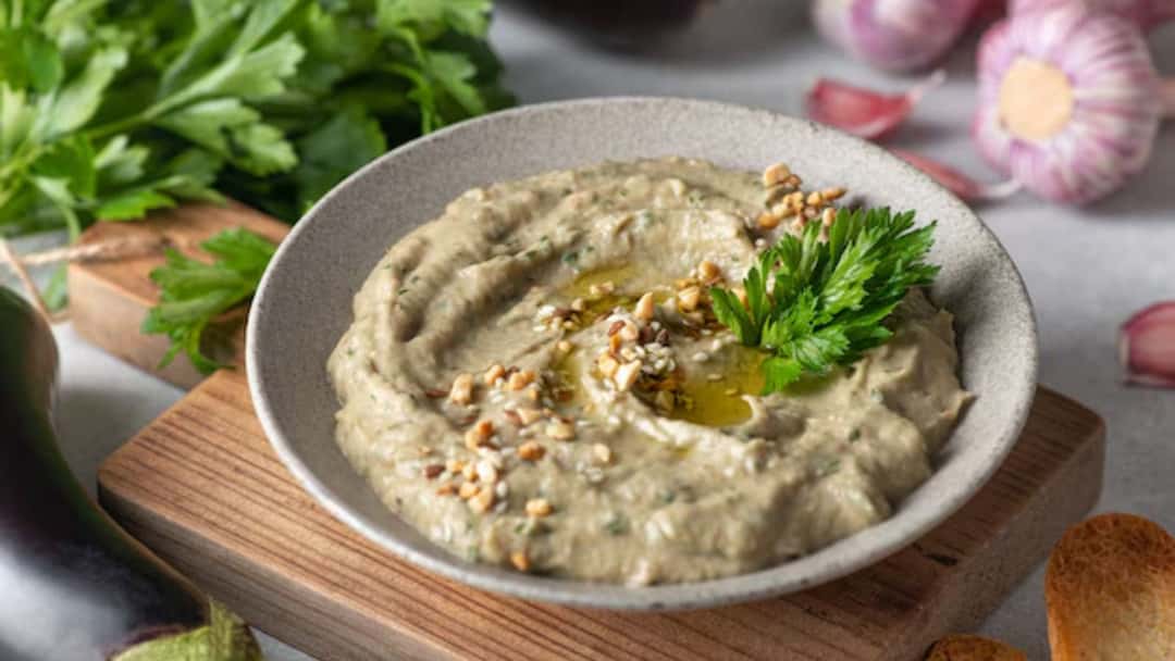 Creamy smoky babaganoush drizzled with olive oil and topped with parsley and paprika in a serving bowl
