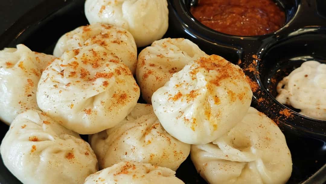 Plate of steamed paneer momos served in traditional wooden boxes