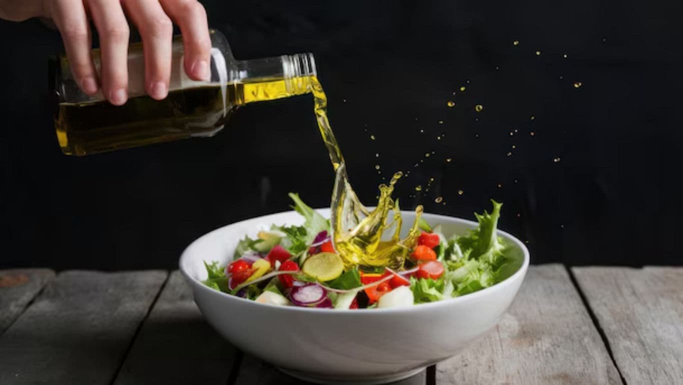 Hand pours olive oil onto fresh vegetable salad