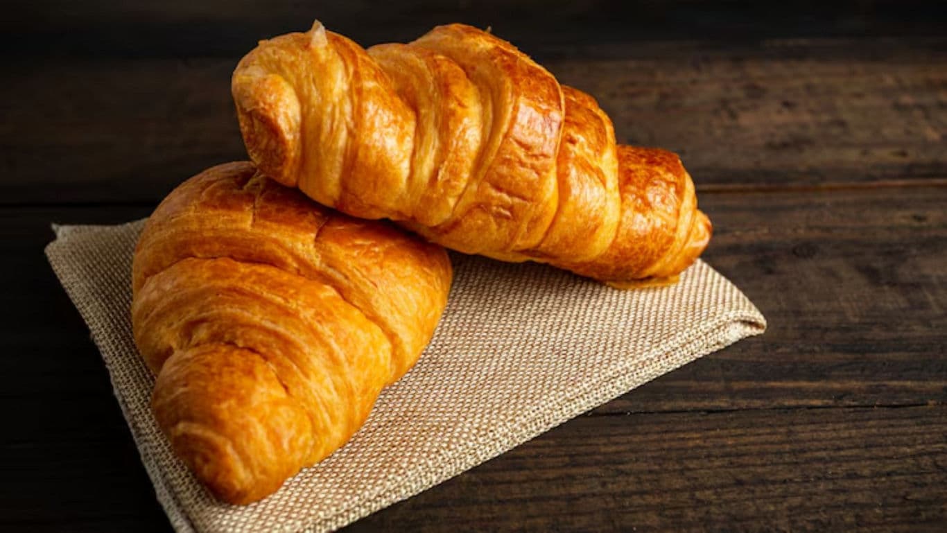 Two golden croissants on rustic wooden table