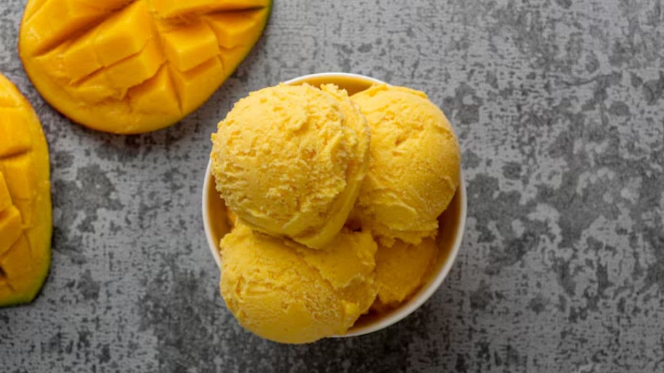 Mango ice cream scoops in bowl with fresh mango