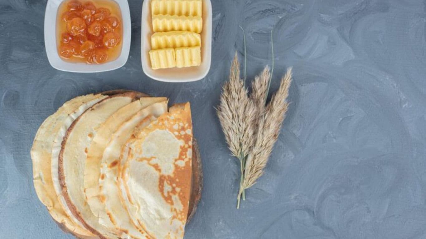 Stack of crepes with butter and jam on table