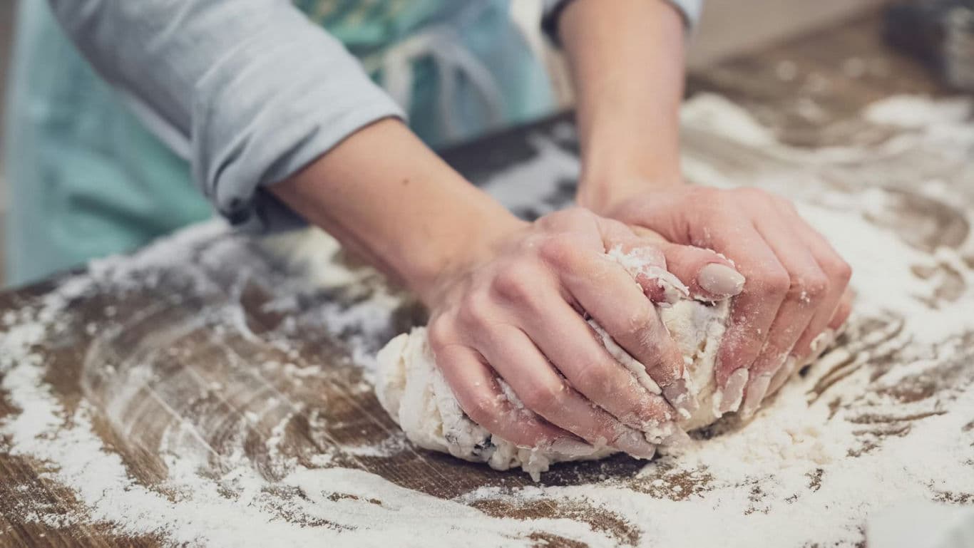 Hands Kneading Dough on Floured Wooden Surface