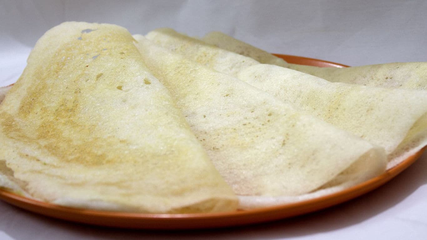 Thin crispy dosas served on orange plate