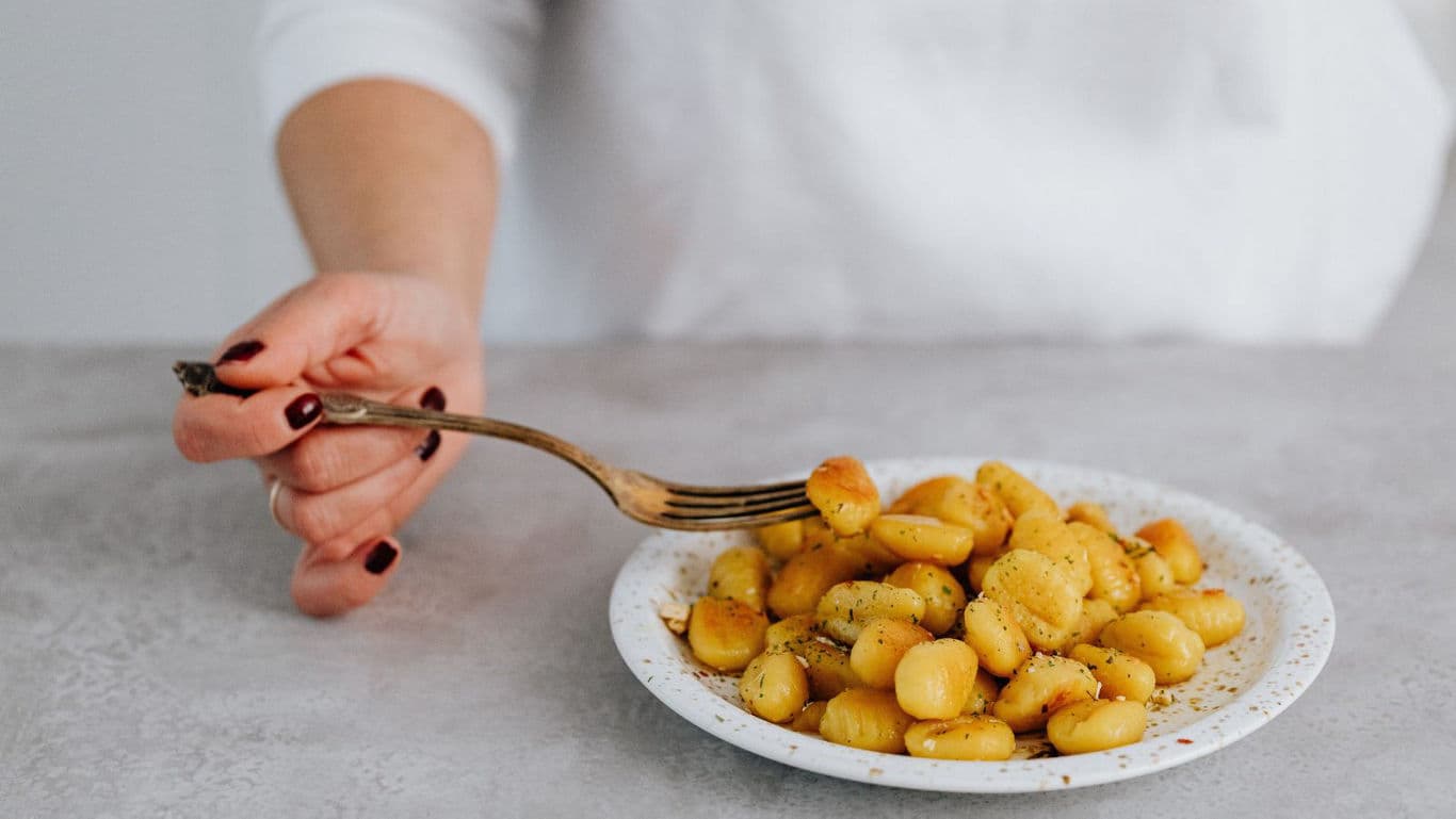 Person eating seasoned gnocchi on plate