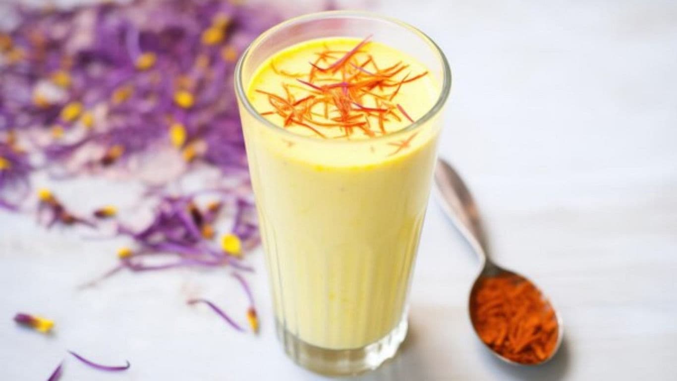 Glass of saffron milkshake on white table