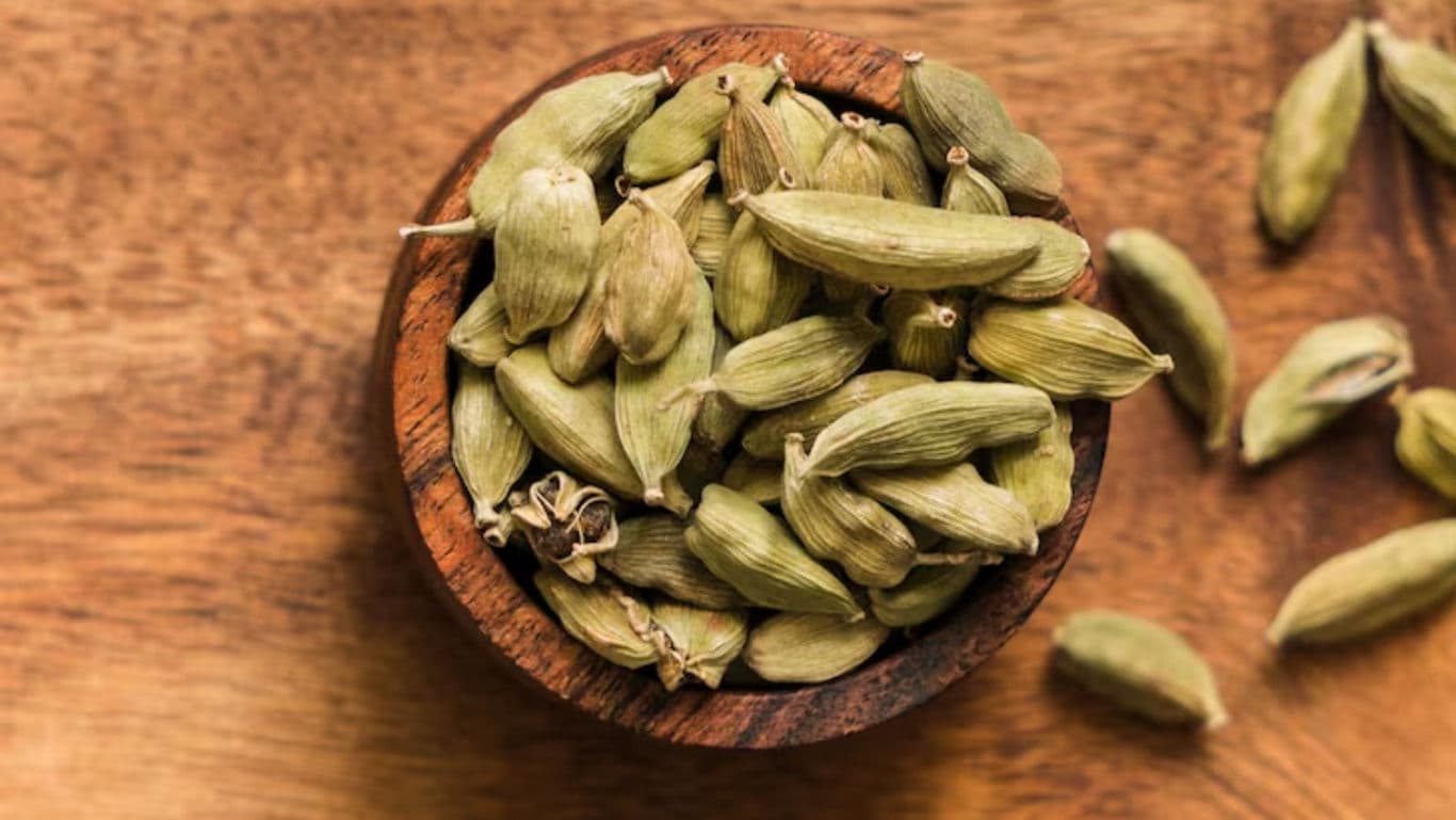 Green cardamom pods in wooden bowl