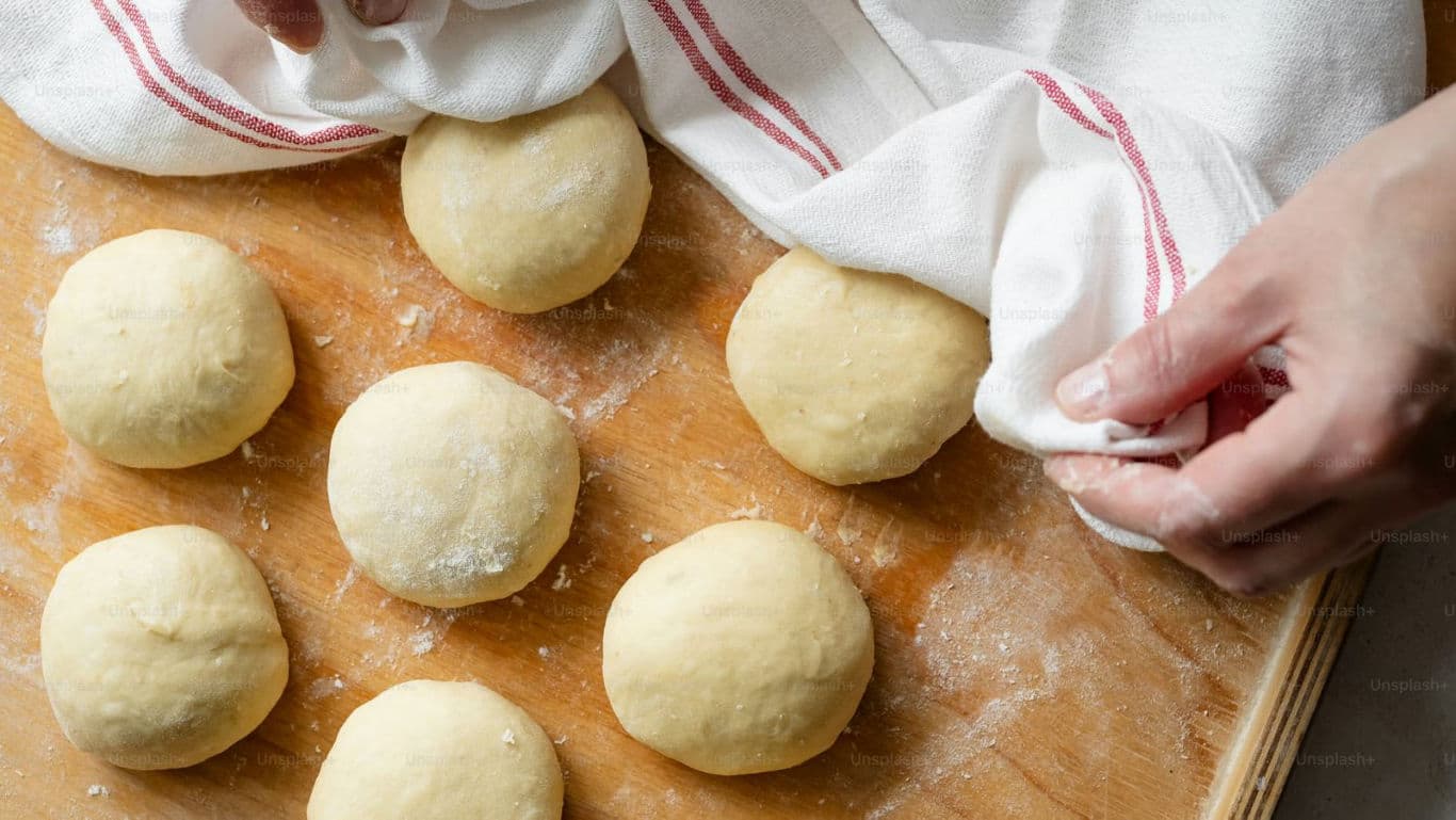 Fresh dough balls resting under kitchen towel