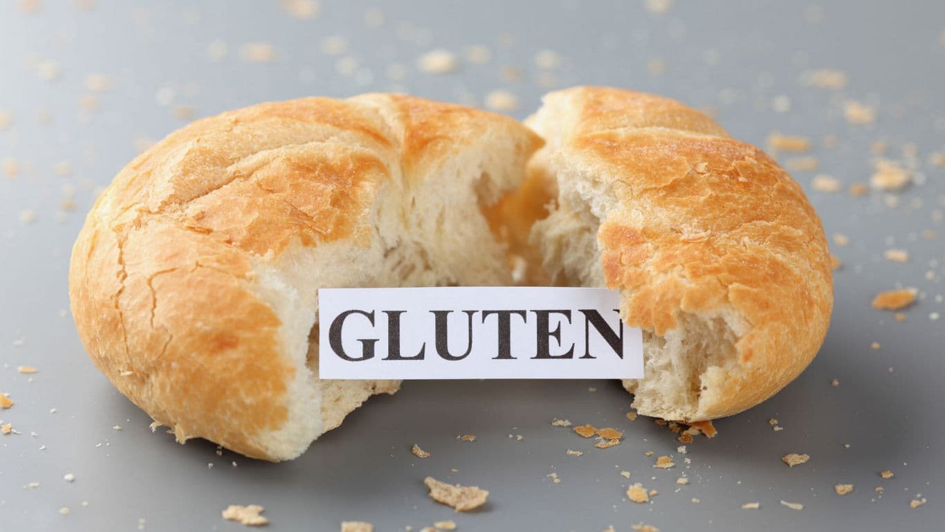 Broken bread roll with gluten label on table
