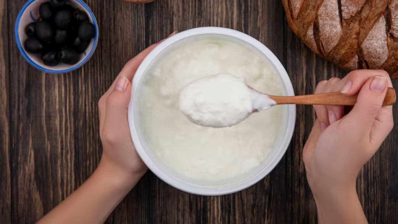 Hands spooning creamy yogurt beside bread