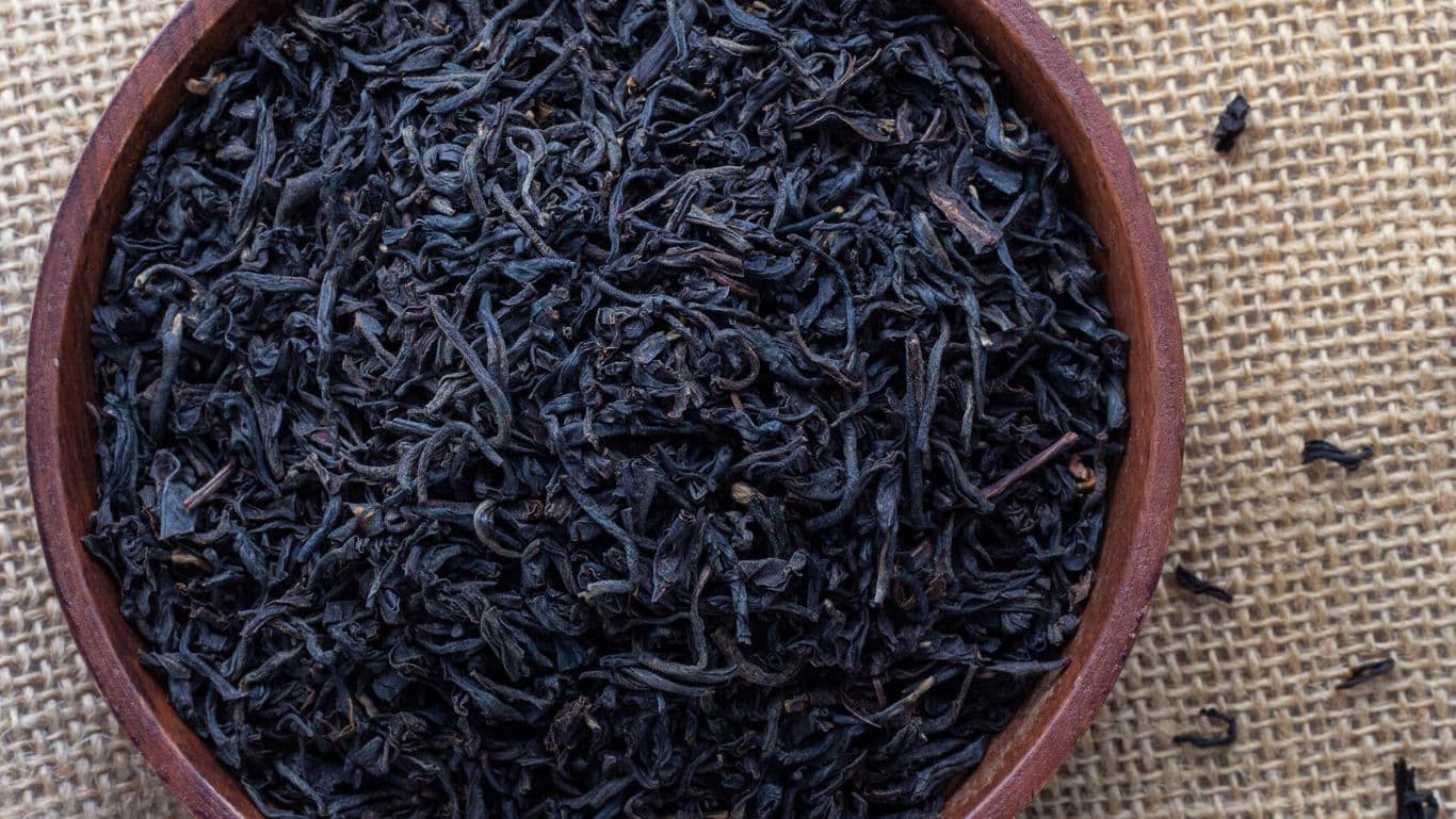 Loose black tea leaves in wooden bowl on burlap