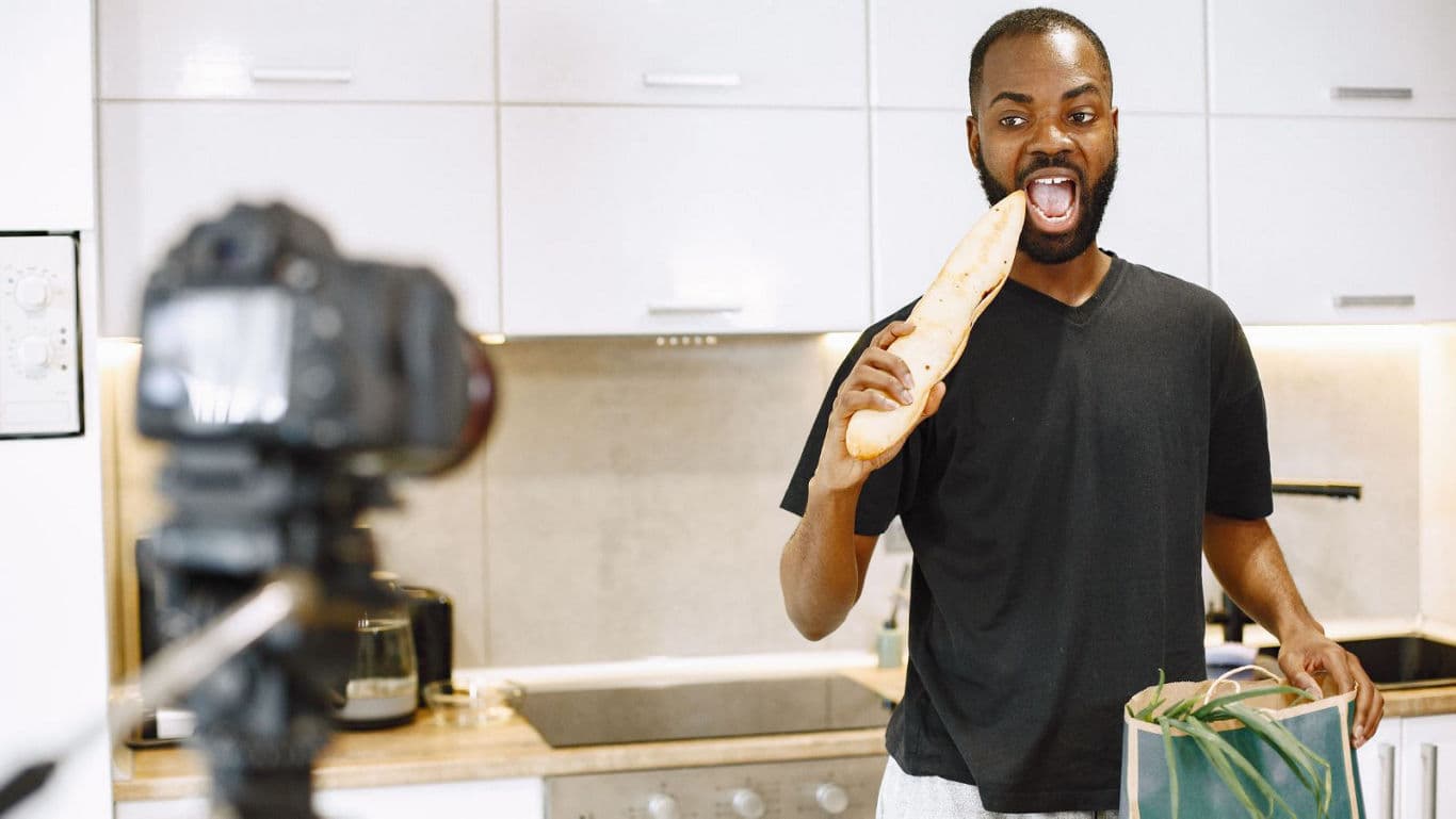Man filming himself eating baguette in kitchen