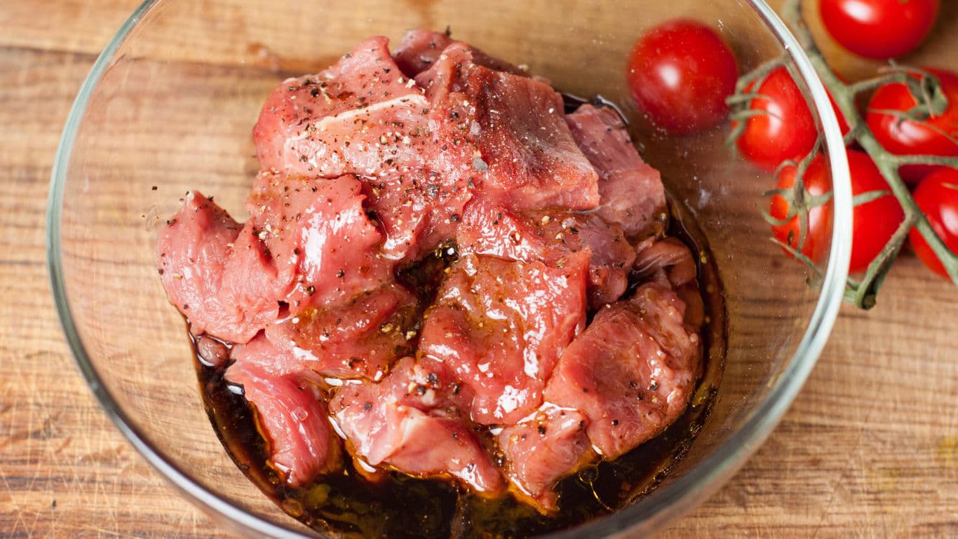 Marinated raw beef cubes in glass bowl on wood