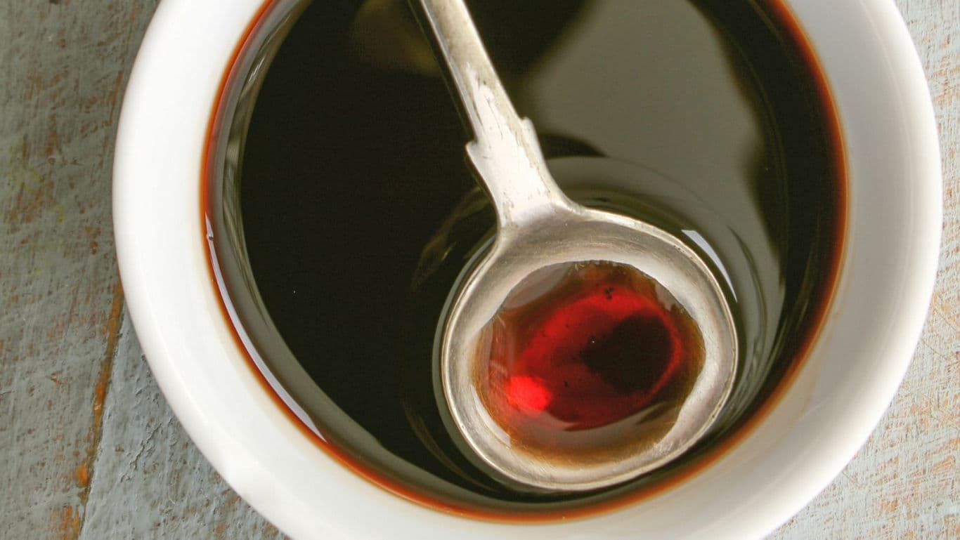 Metal ladle resting in dark sauce bowl