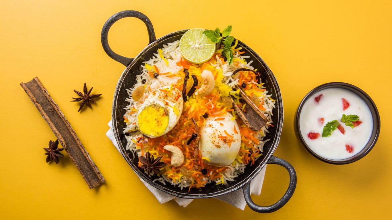 Egg biryani served with yogurt on yellow background