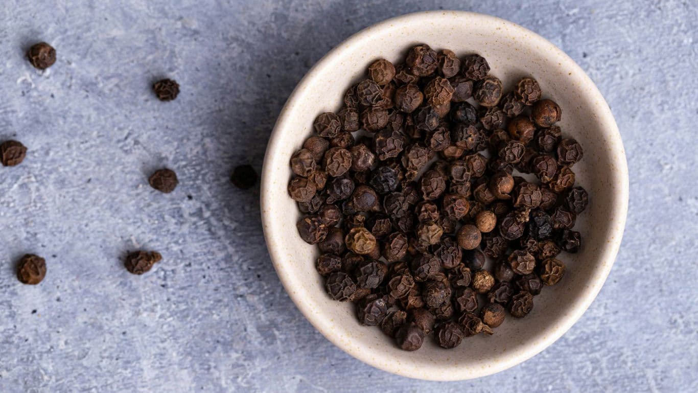 Bowl of whole black peppercorns on stone