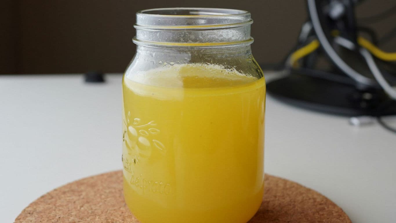 Glass mason jar filled with yellow juice on cork mat