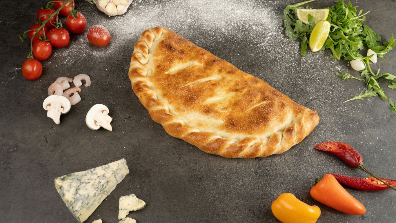 Baked calzone surrounded by fresh ingredients
