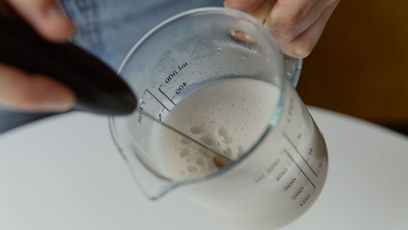 Person frothing milk in measuring jug