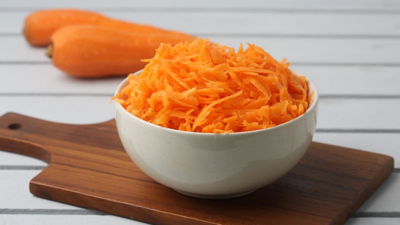 Bowl of freshly grated carrots on wooden board