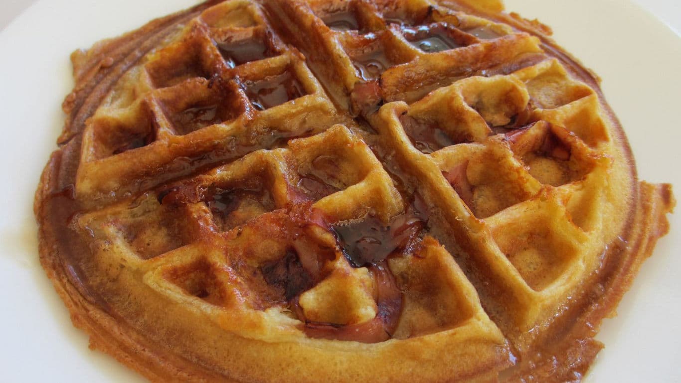 Golden waffle with syrup on white plate