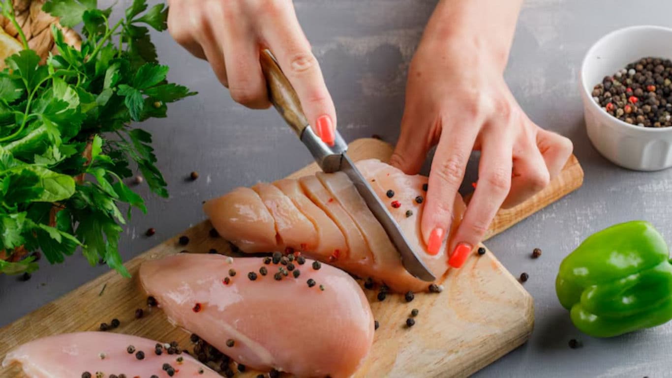 Slicing Raw Chicken Breast with Fresh Herbs Nearby