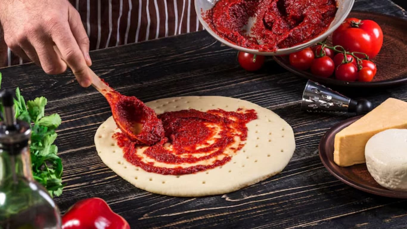 Person Spreading Tomato Sauce on Pizza Dough