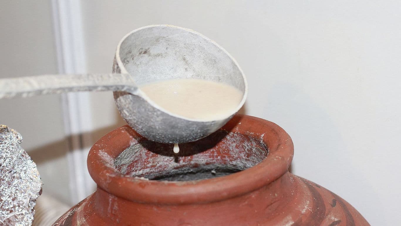 Ladle pouring liquid into traditional clay pot