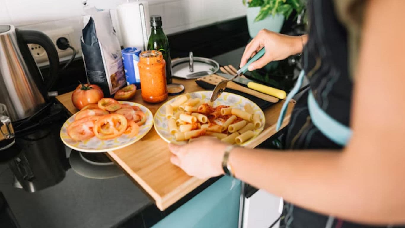Person Preparing Pasta with Tomato Sauce in Kitchen