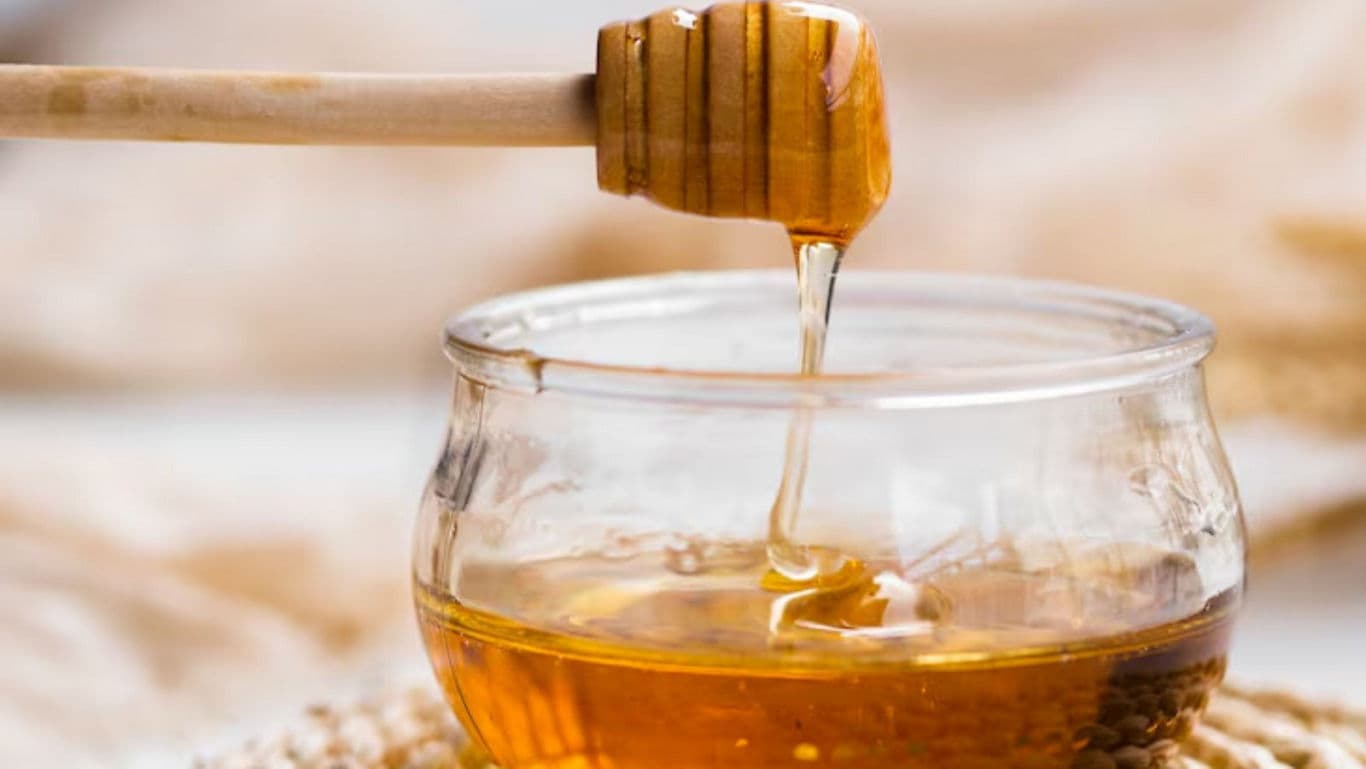 Honey Dripping from Wooden Dipper into Glass Jar