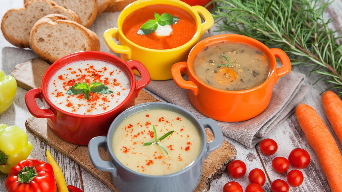 4 soup bowls on a table with vegetables on the side