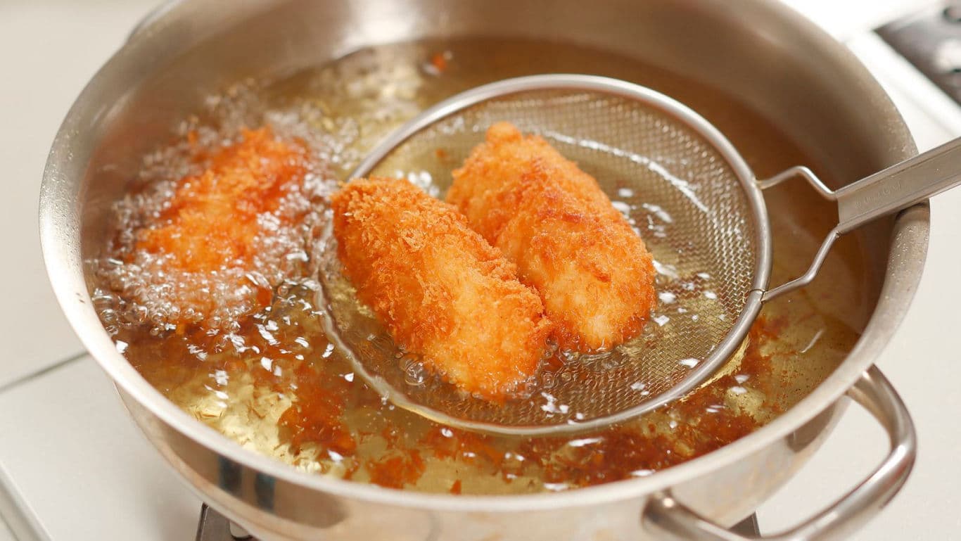 Golden breaded croquettes deep frying in pan