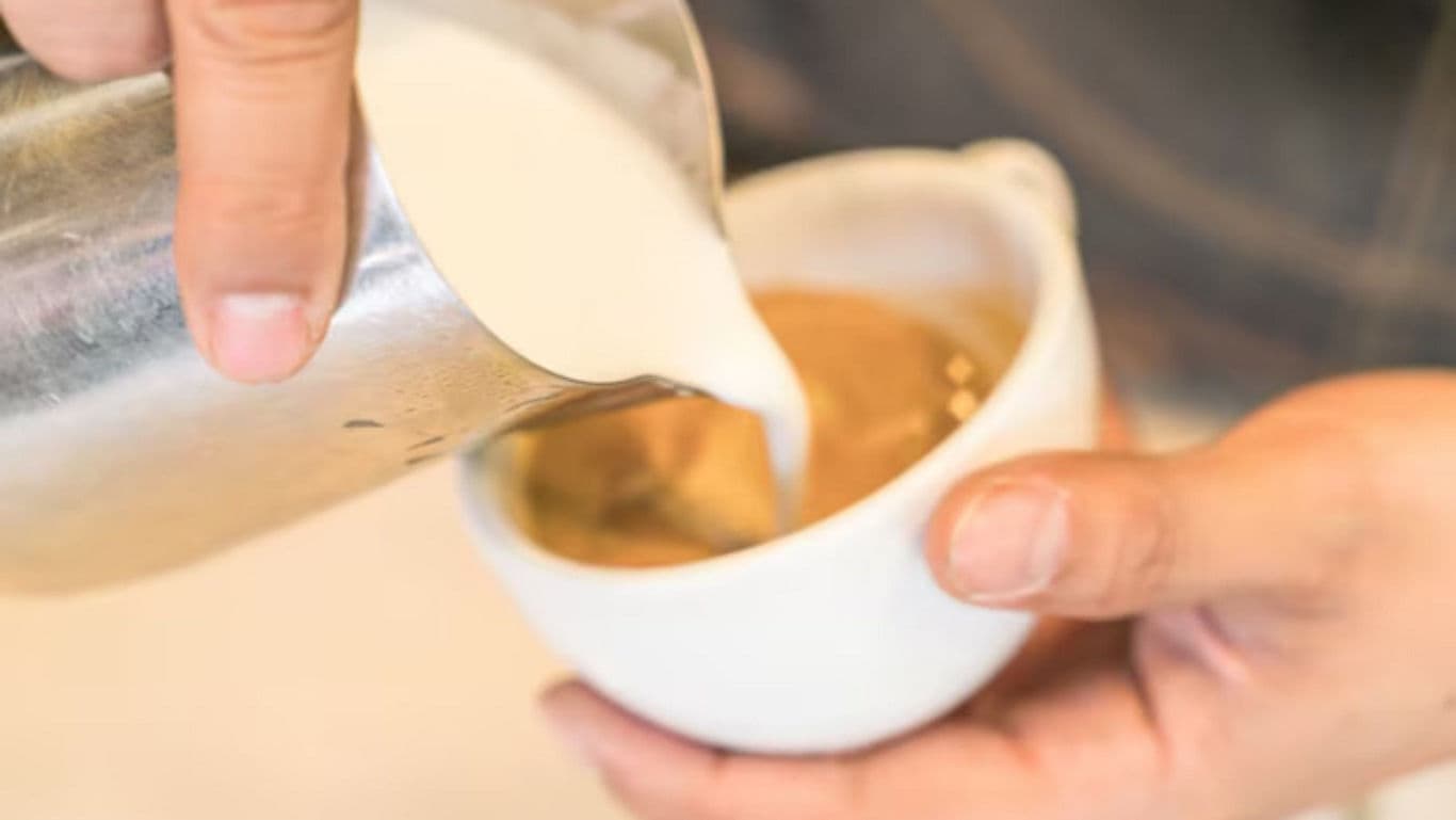 Barista pouring milk into hot coffee