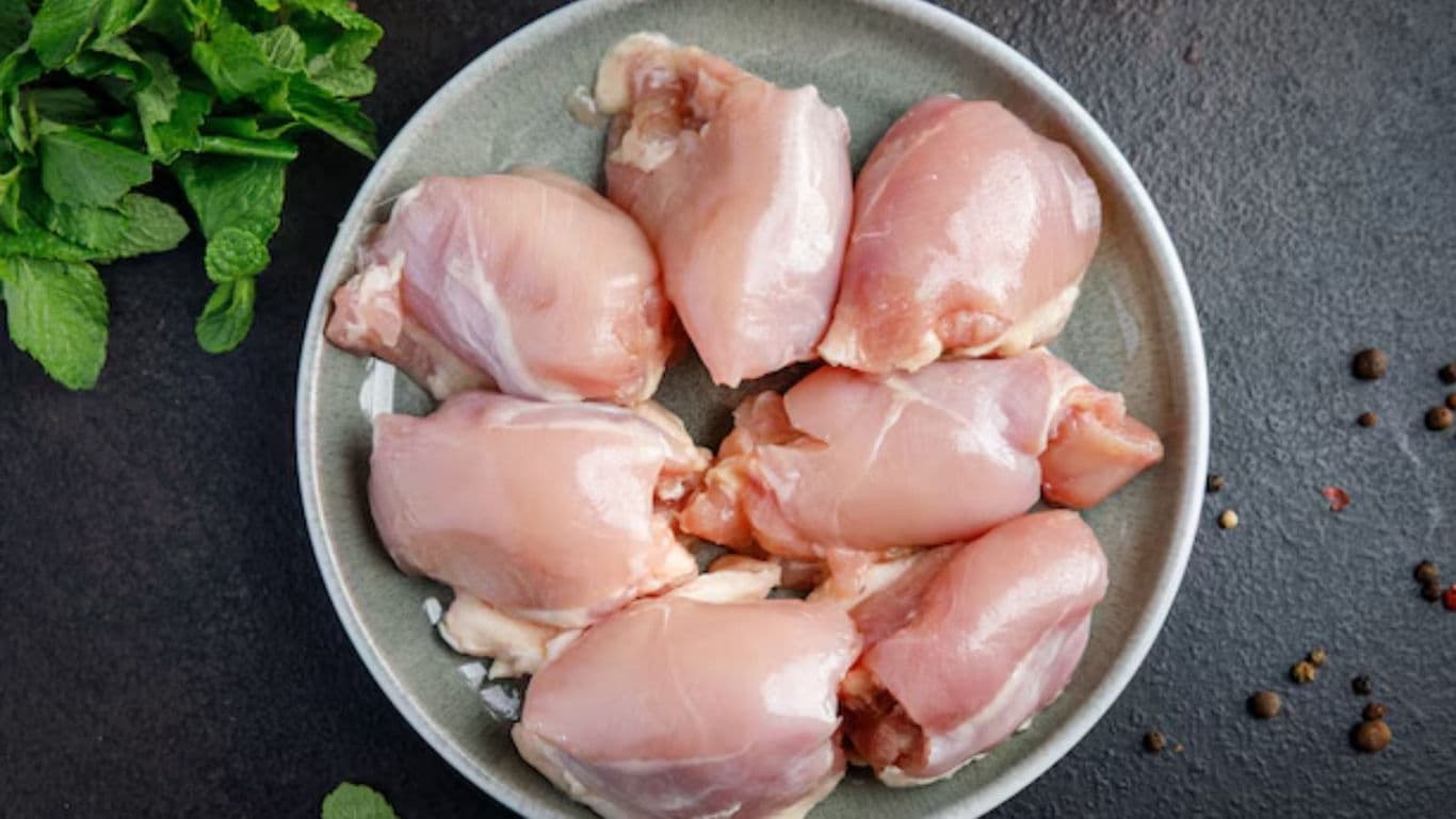 Raw chicken thighs on ceramic plate with herbs