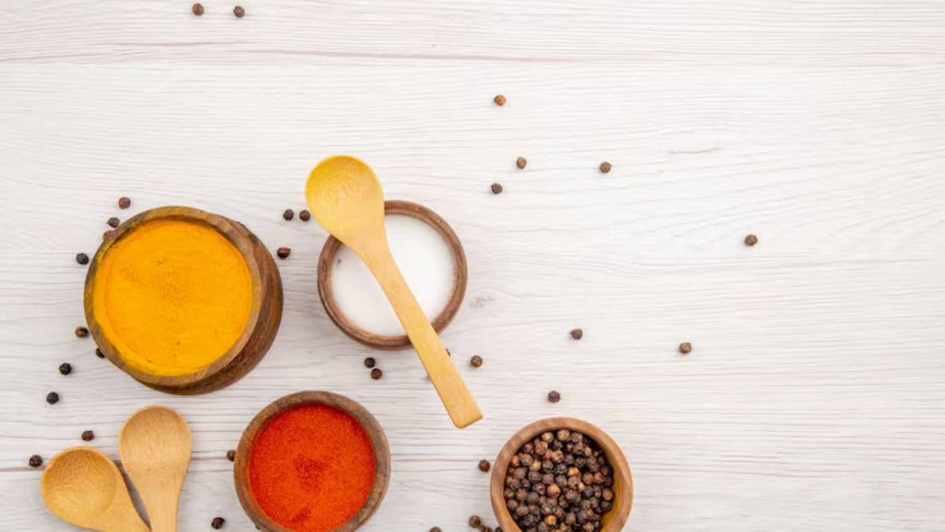 Assorted spices in wooden bowls on white table