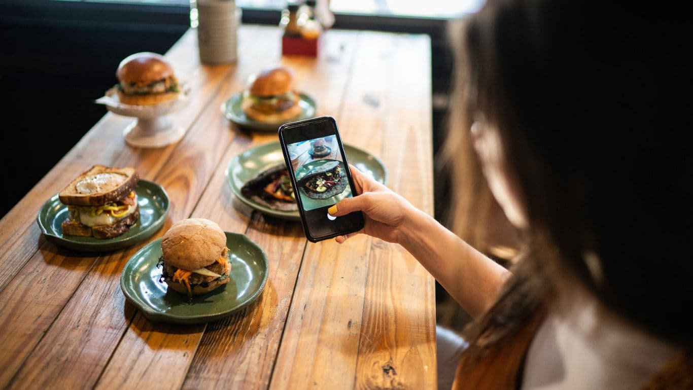 Woman photographing gourmet burgers with smartphone