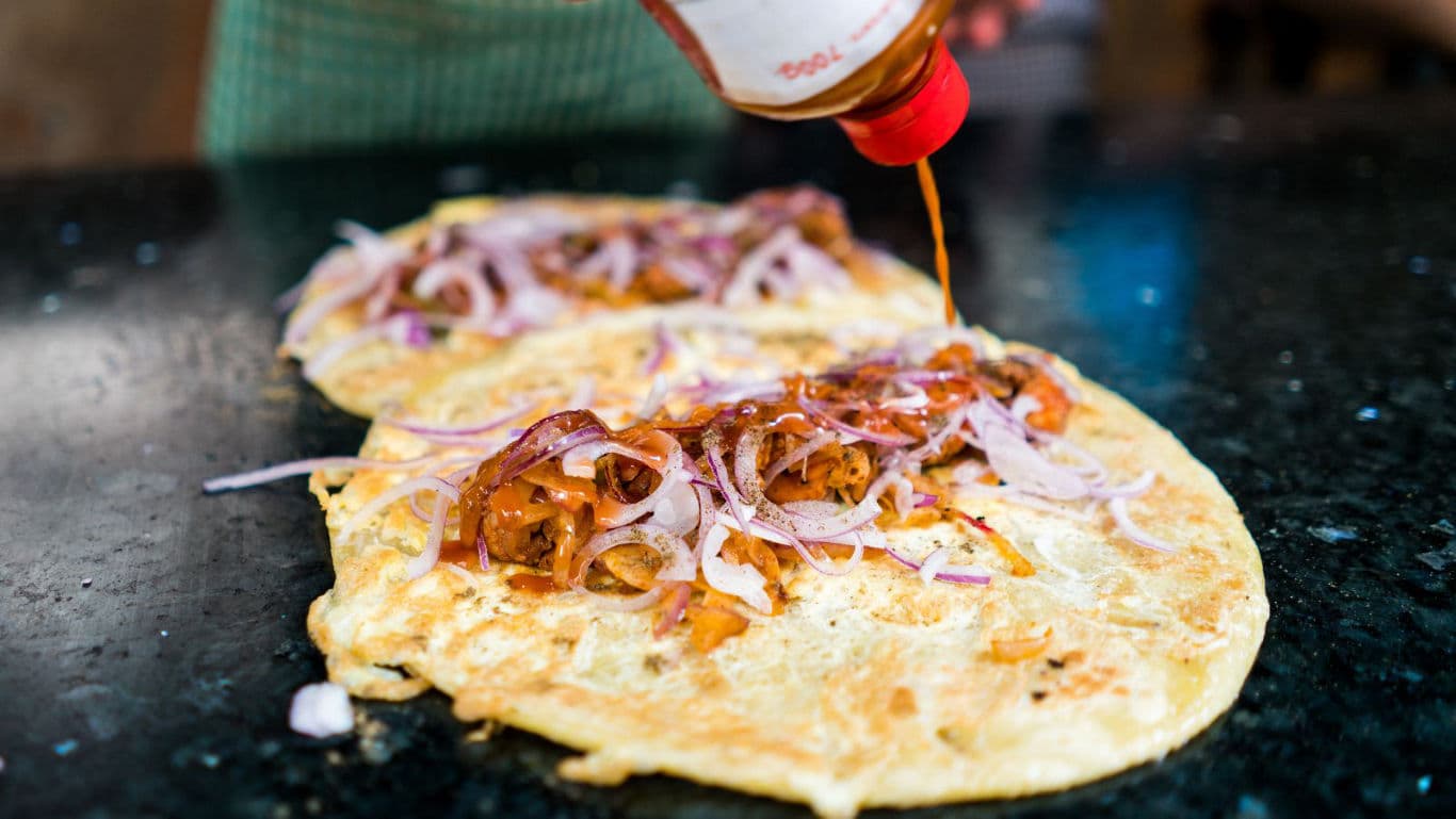 Street vendor preparing spicy egg dosa wraps