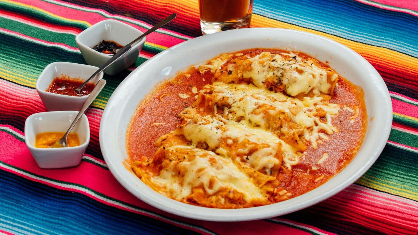 Cheesy enchiladas with sauces on colorful tablecloth