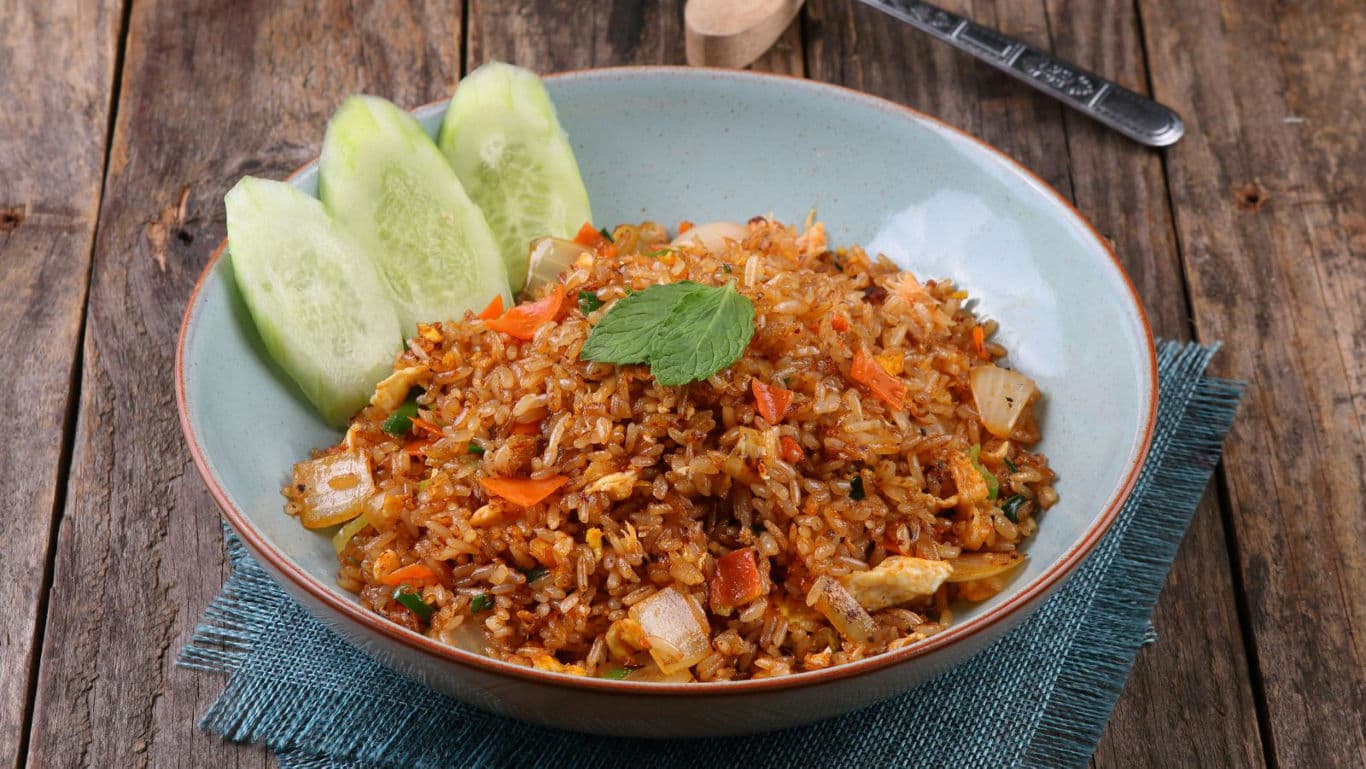 Bowl of fried rice with cucumber slices on wood