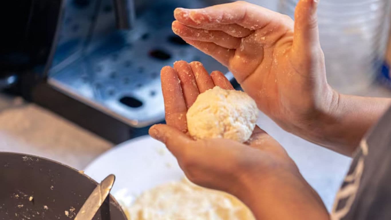 Person shaping dough ball in kitchen setting