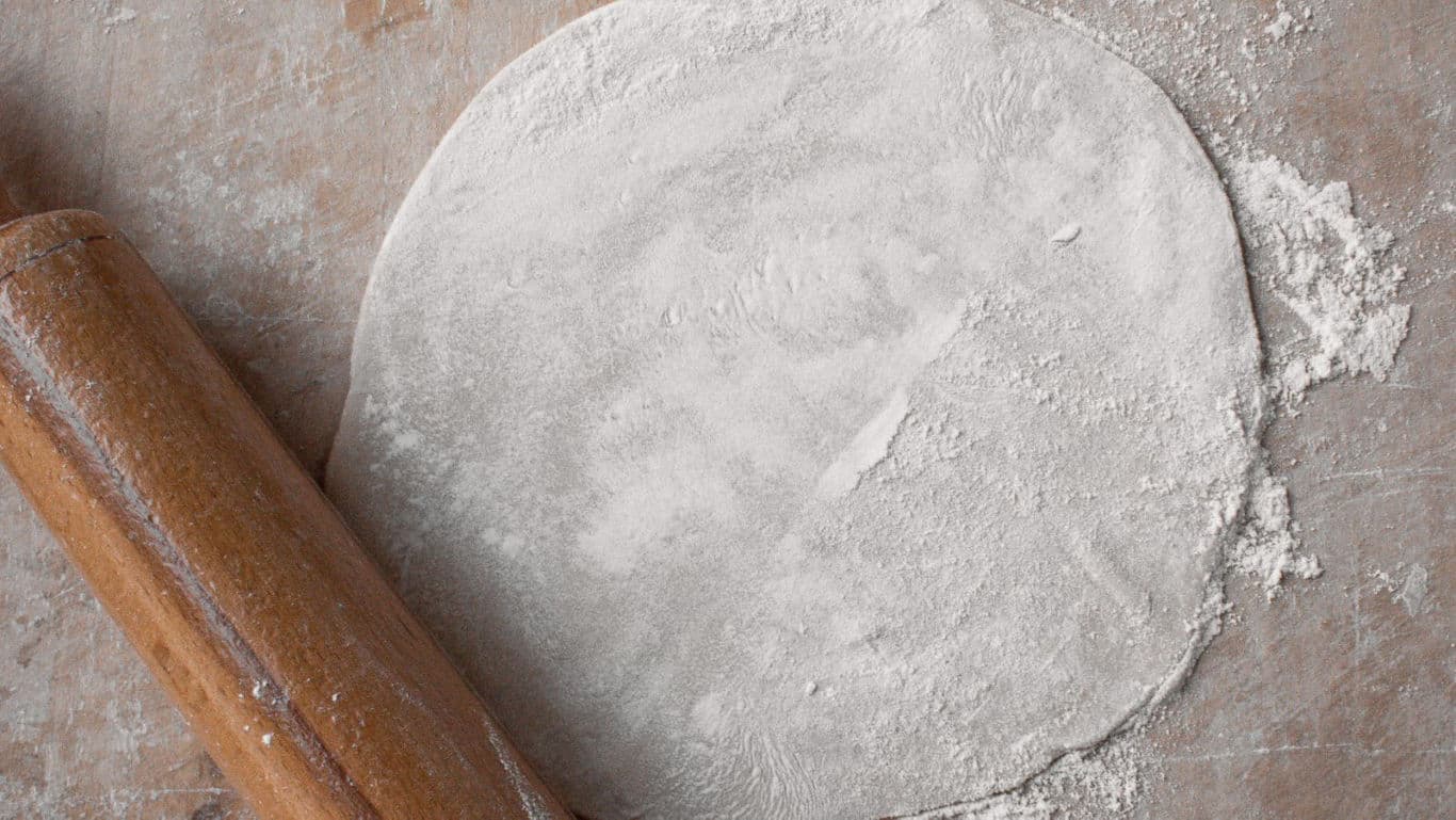 Floured dough circle with wooden rolling pin