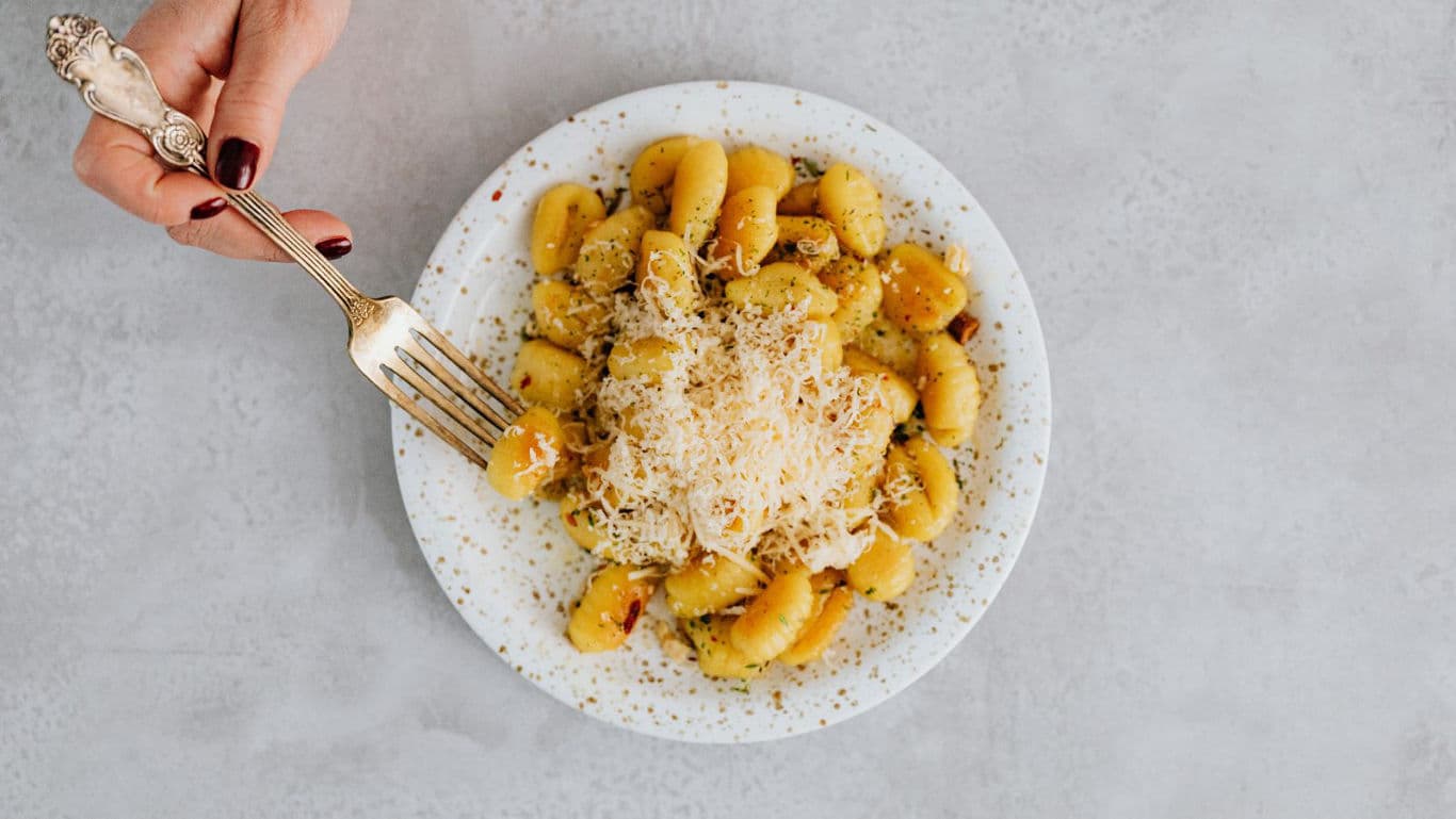 Hand holding fork over plate of gnocchi with cheese