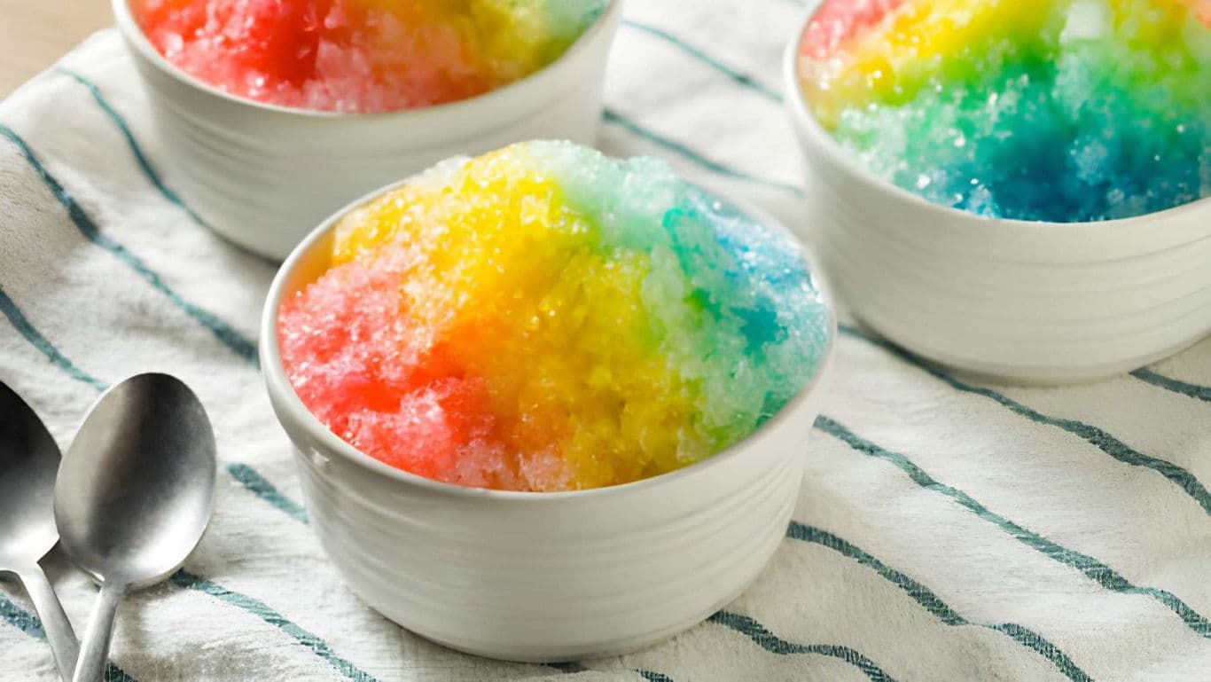 A bowl of colourful shaved ice dessert topped with rainbow syrups