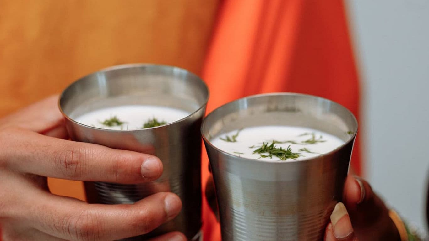 Two hands holding steel cups of spiced yogurt drink